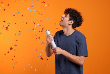 Photo of Emotional young man blowing up party popper on orange background