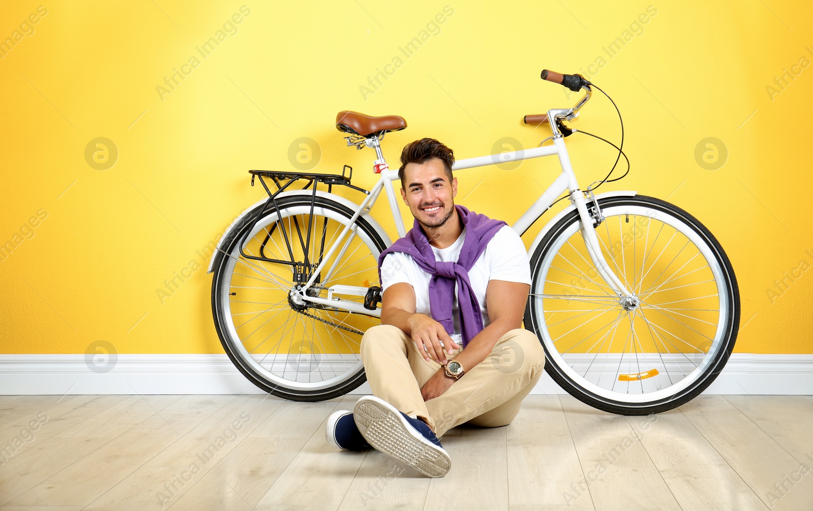Photo of Handsome young hipster man sitting with bicycle near yellow wall