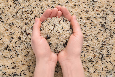 Photo of Woman holding mix of brown and polished rice over grains, top view