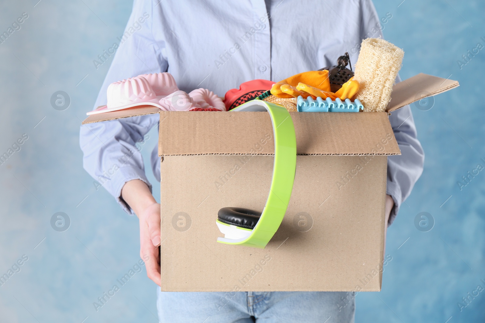 Photo of Woman holding box of unwanted stuff on blue background, closeup