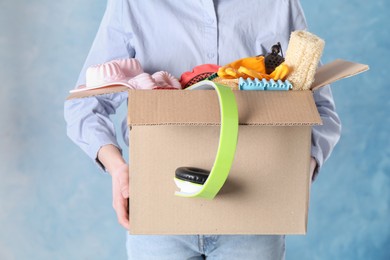 Woman holding box of unwanted stuff on blue background, closeup
