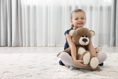 Photo of Cute little girl playing with teddy bear at home. Space for text