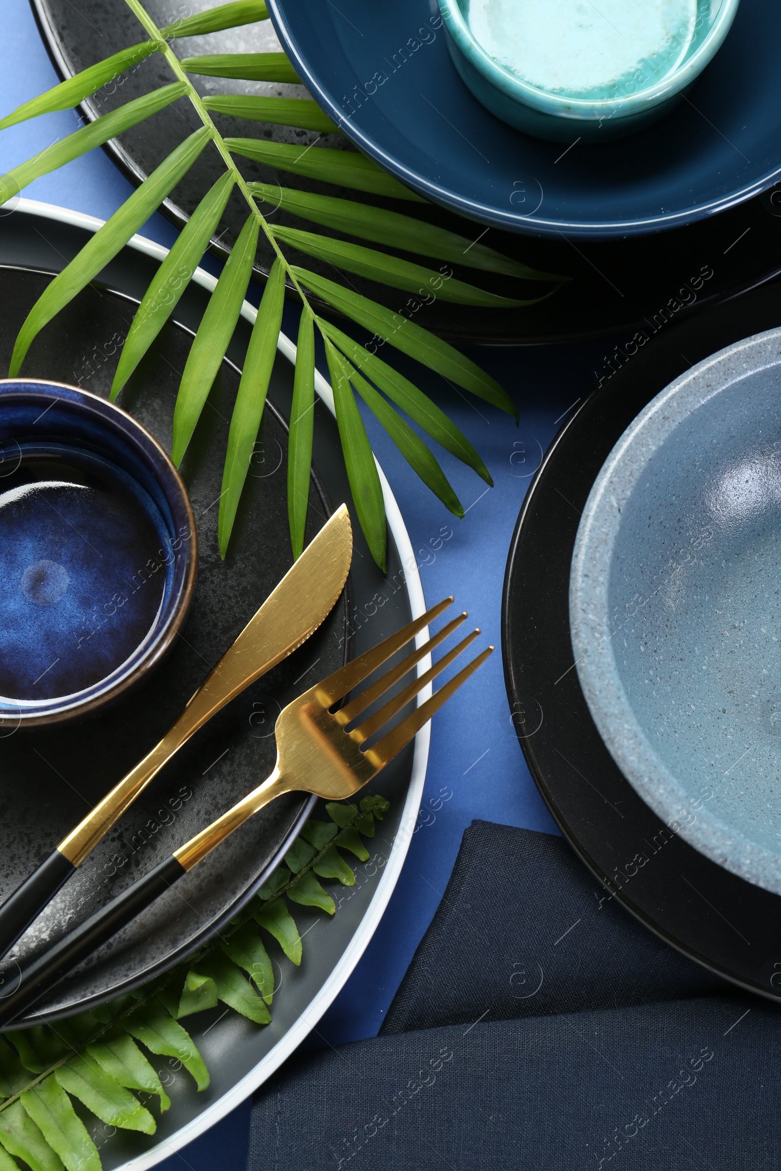 Photo of Flat lay composition with stylish ceramic plates and floral decor on blue background