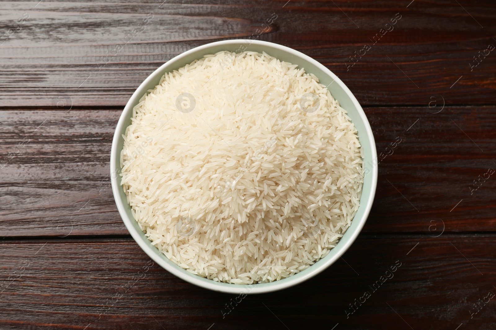 Photo of Raw basmati rice in bowl on wooden table, top view