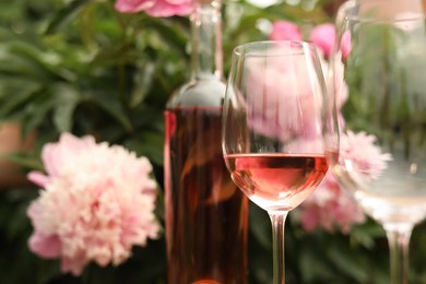 Photo of Glasses and bottle with rose wine against beautiful peonies, closeup. Space for text