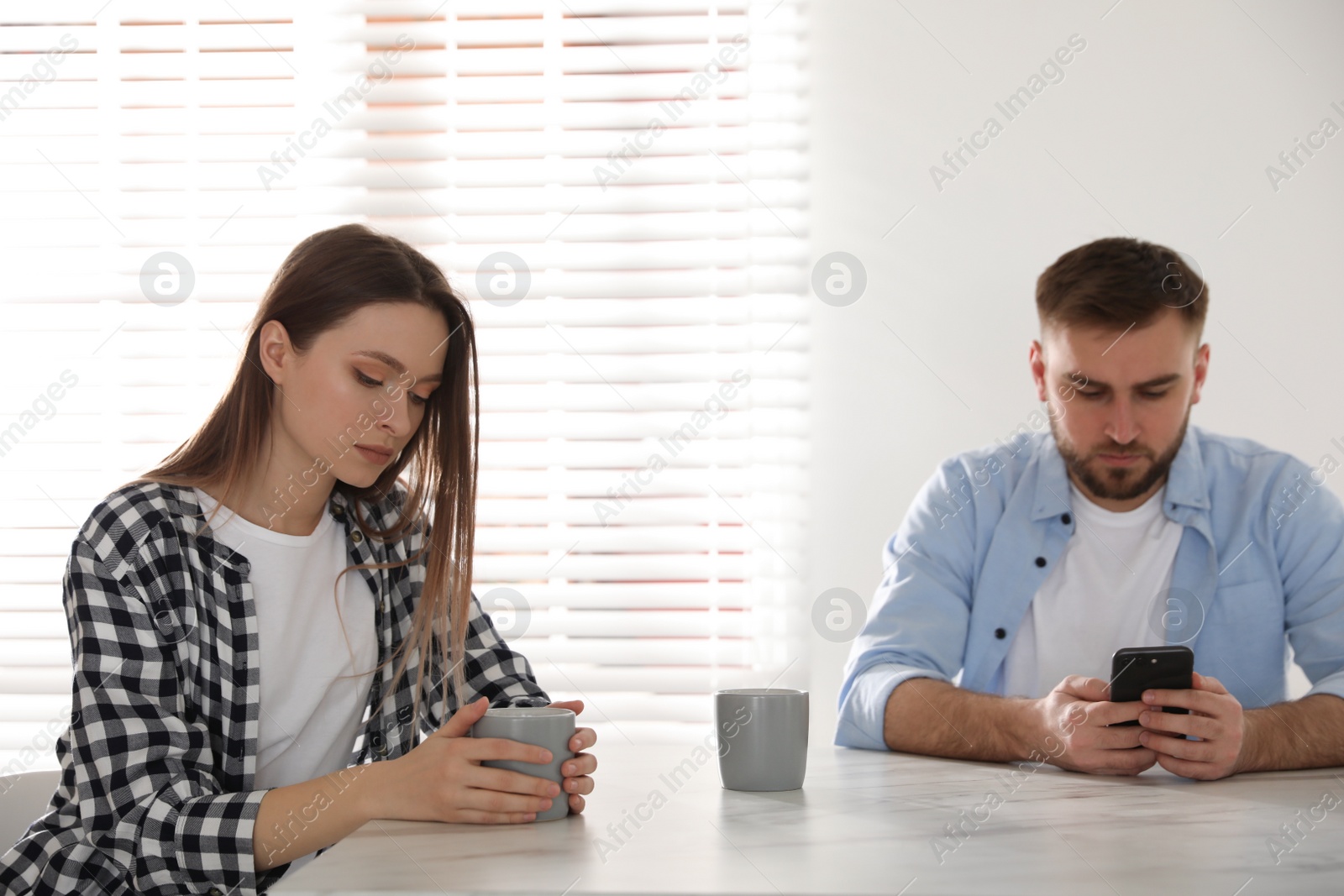 Photo of Young man preferring smartphone over his girlfriend at home. Relationship problems