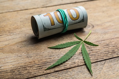 Photo of Hemp leaf and rolled money on wooden background, closeup