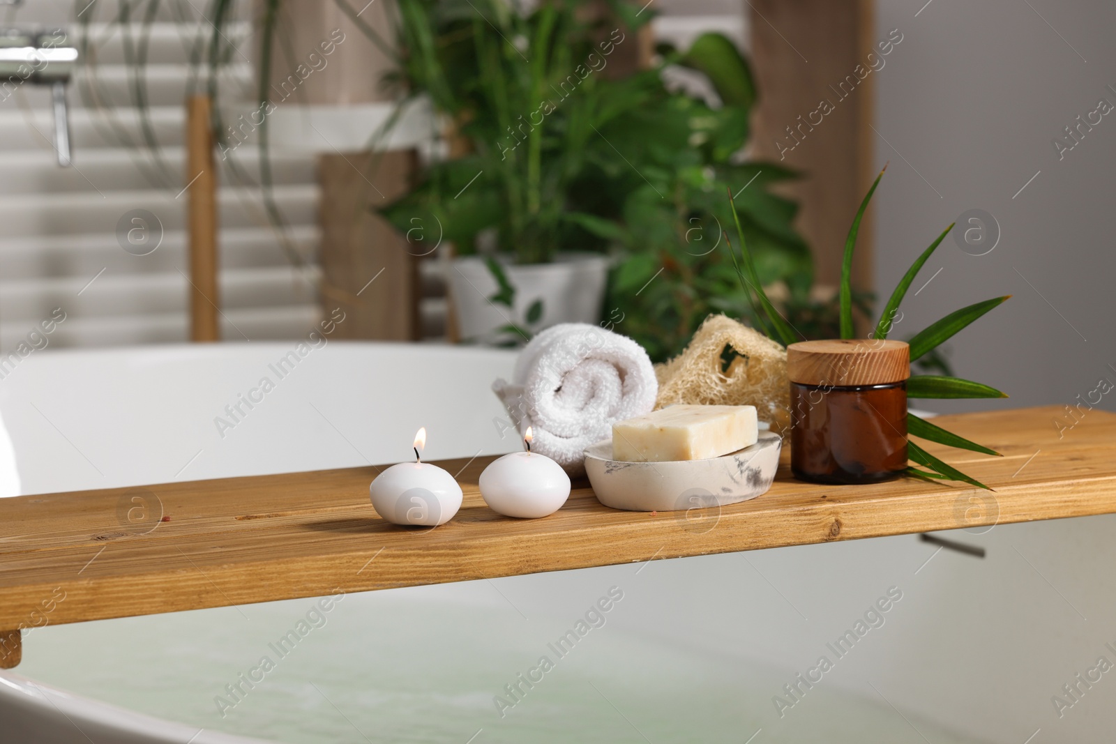 Photo of Wooden board with spa products on bath tub in bathroom, space for text