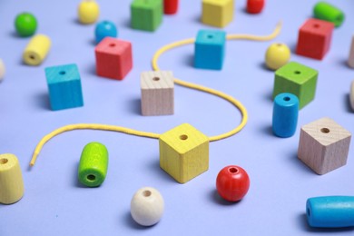 Wooden pieces and string for threading activity on violet background, closeup. Educational toy for motor skills development