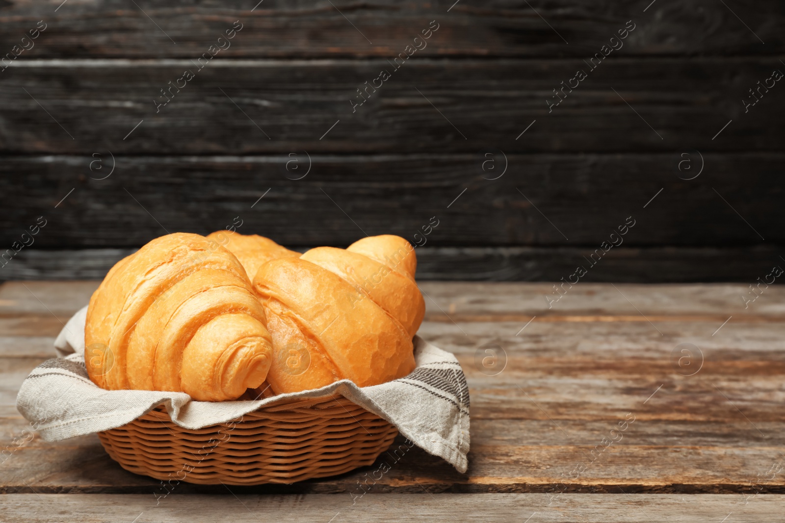 Photo of Basket with tasty croissants on wooden table
