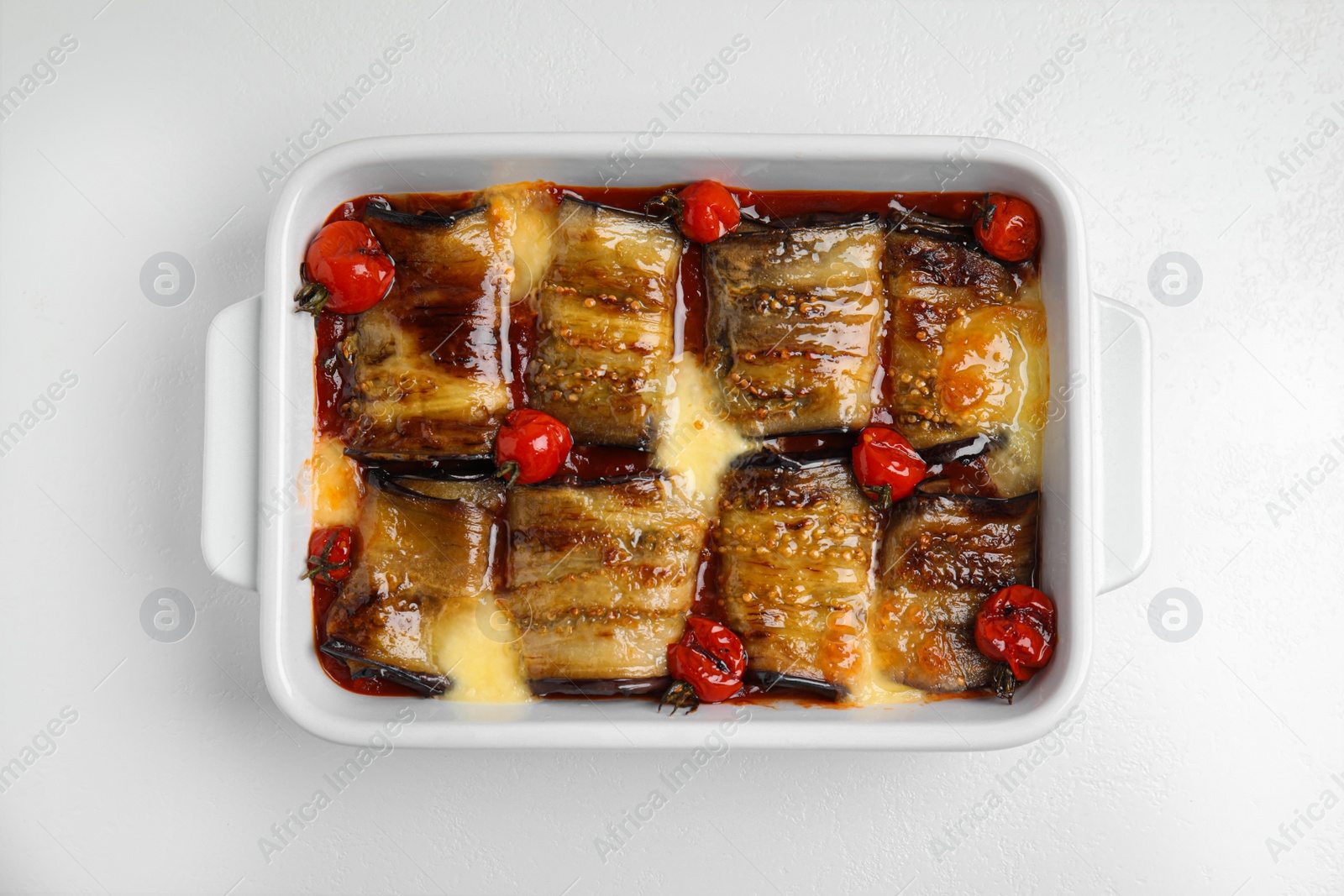 Photo of Tasty eggplant rolls with tomatoes and cheese in baking dish on white table, top view