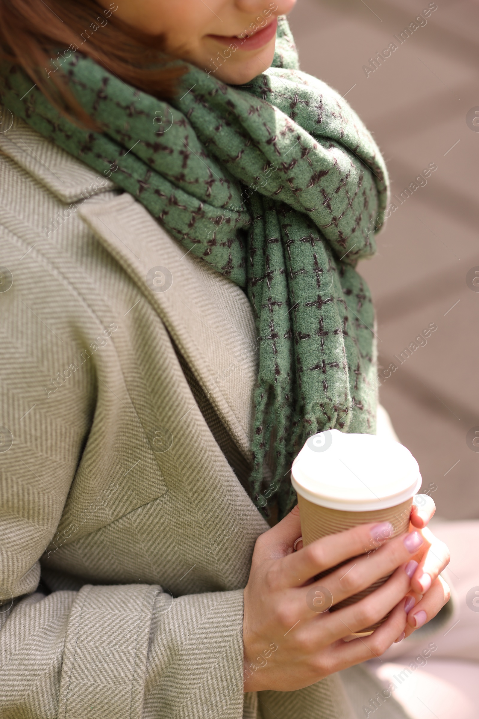 Photo of Beautiful woman in warm scarf with paper cup of coffee outdoors, closeup