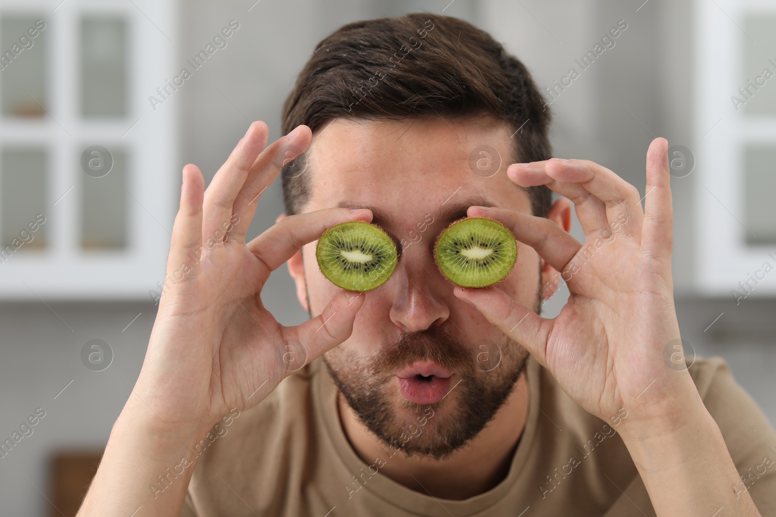 Photo of Man covering his eyes with halves of kiwi in kitchen