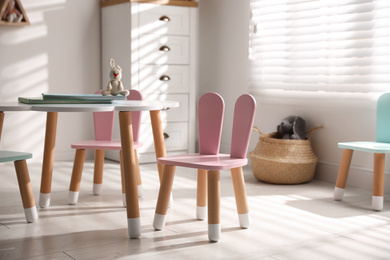 Photo of Small table and chairs with bunny ears in children's room interior