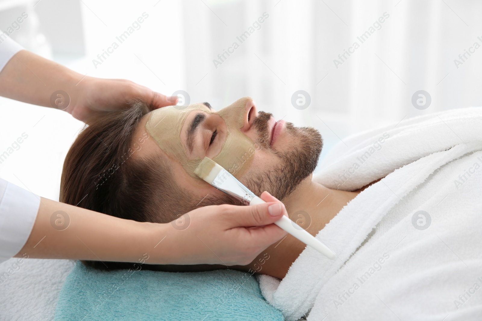 Photo of Cosmetologist applying mask on client's face in spa salon