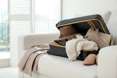 Photo of Open suitcase full of clothes, jacket and fashionable shoes on sofa in room
