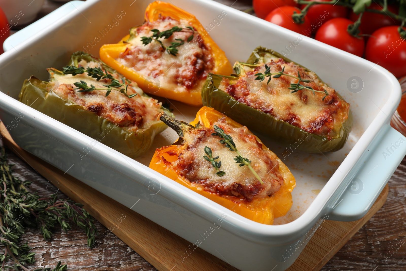 Photo of Tasty stuffed peppers in dish and ingredients on wooden table, closeup