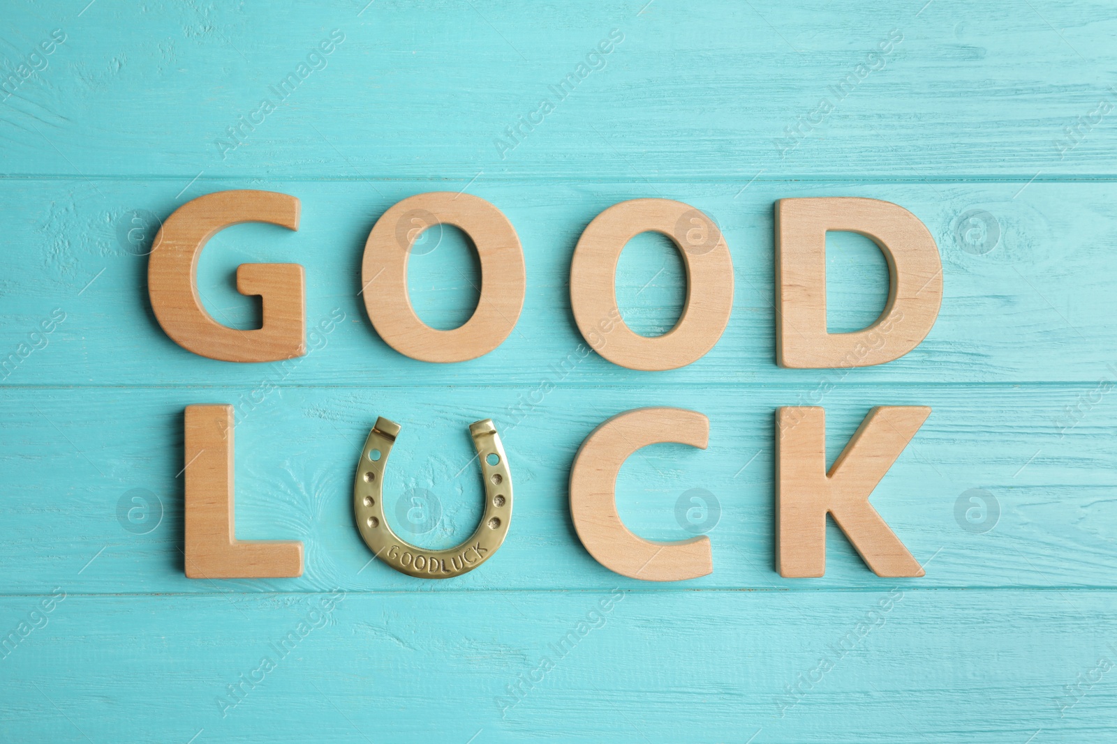 Photo of Phrase GOOD LUCK made of wooden letters and horseshoe on light blue table, flat lay