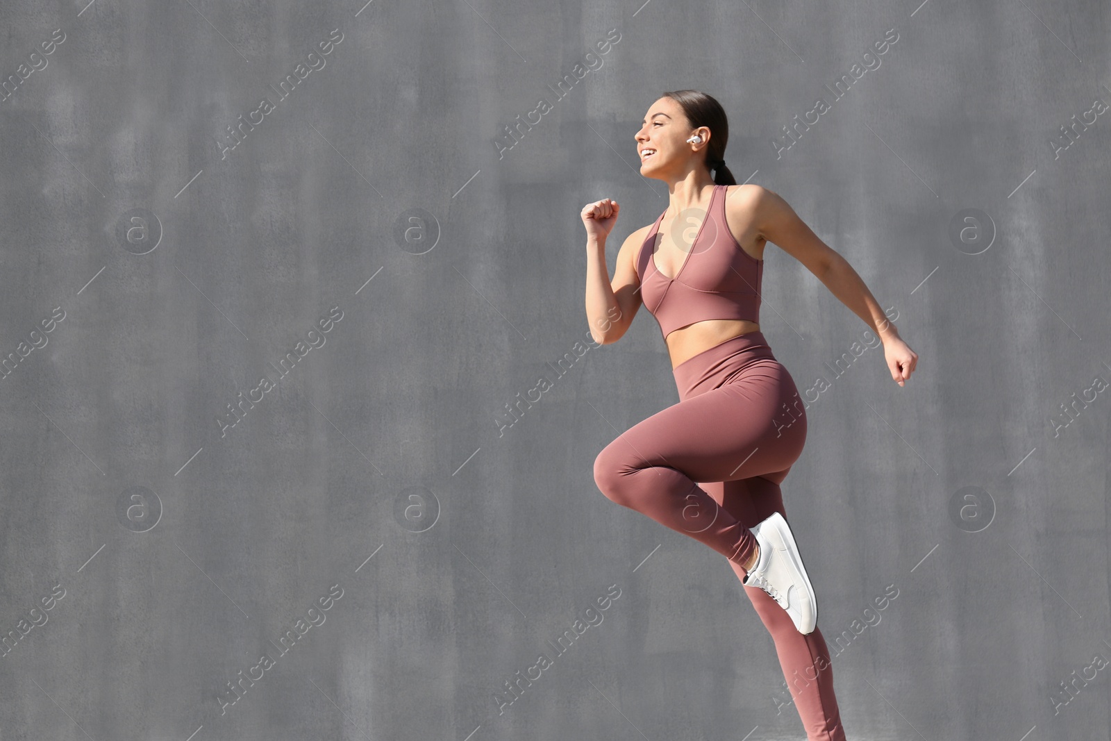 Photo of Happy young woman in stylish sports wear jumping on grey background. Space for text