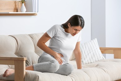 Photo of Young woman suffering from menstrual pain on sofa at home