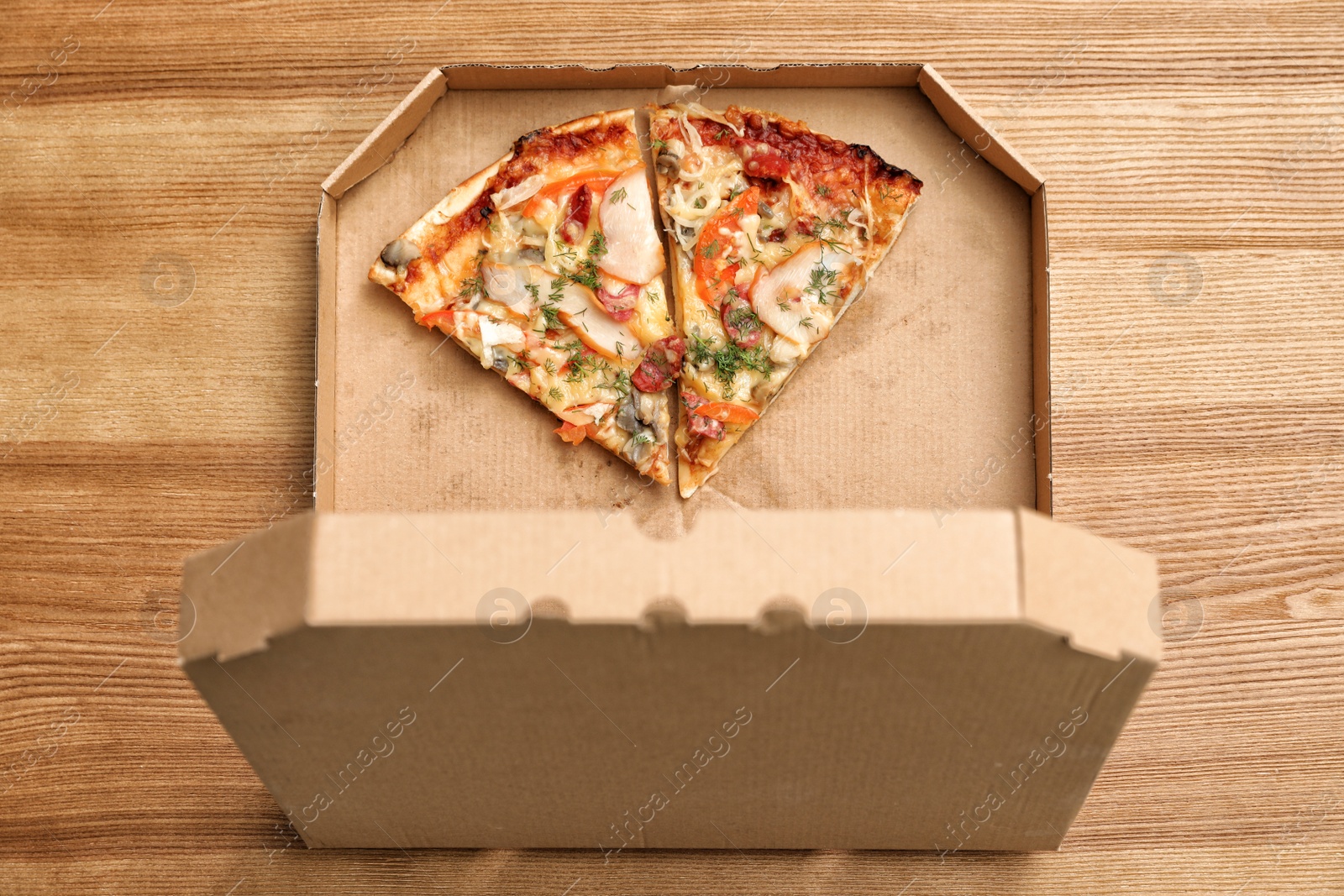 Photo of Cardboard box with pizza pieces on wooden background, top view