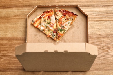 Cardboard box with pizza pieces on wooden background, top view