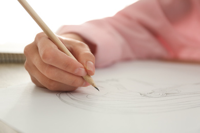 Woman drawing girl's portrait with pencil on sheet of paper at table, closeup