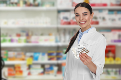 Professional pharmacist with pills in modern drugstore, space for text 