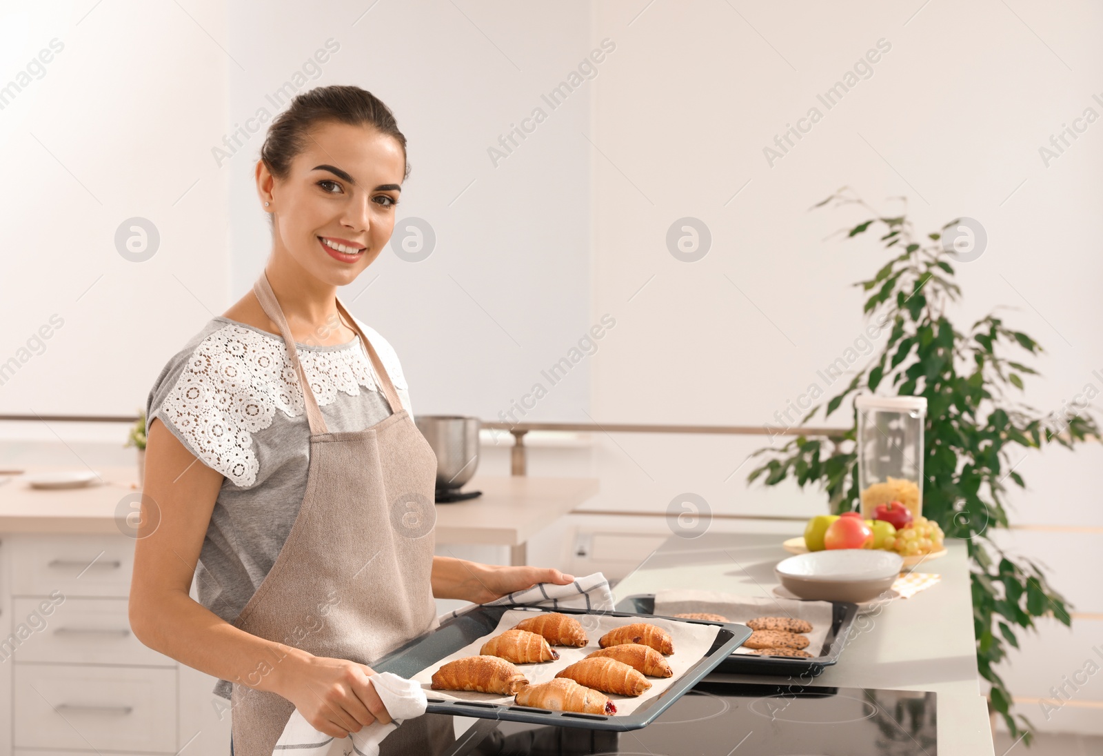 Photo of Young woman holding oven sheet with homemade croissants in kitchen