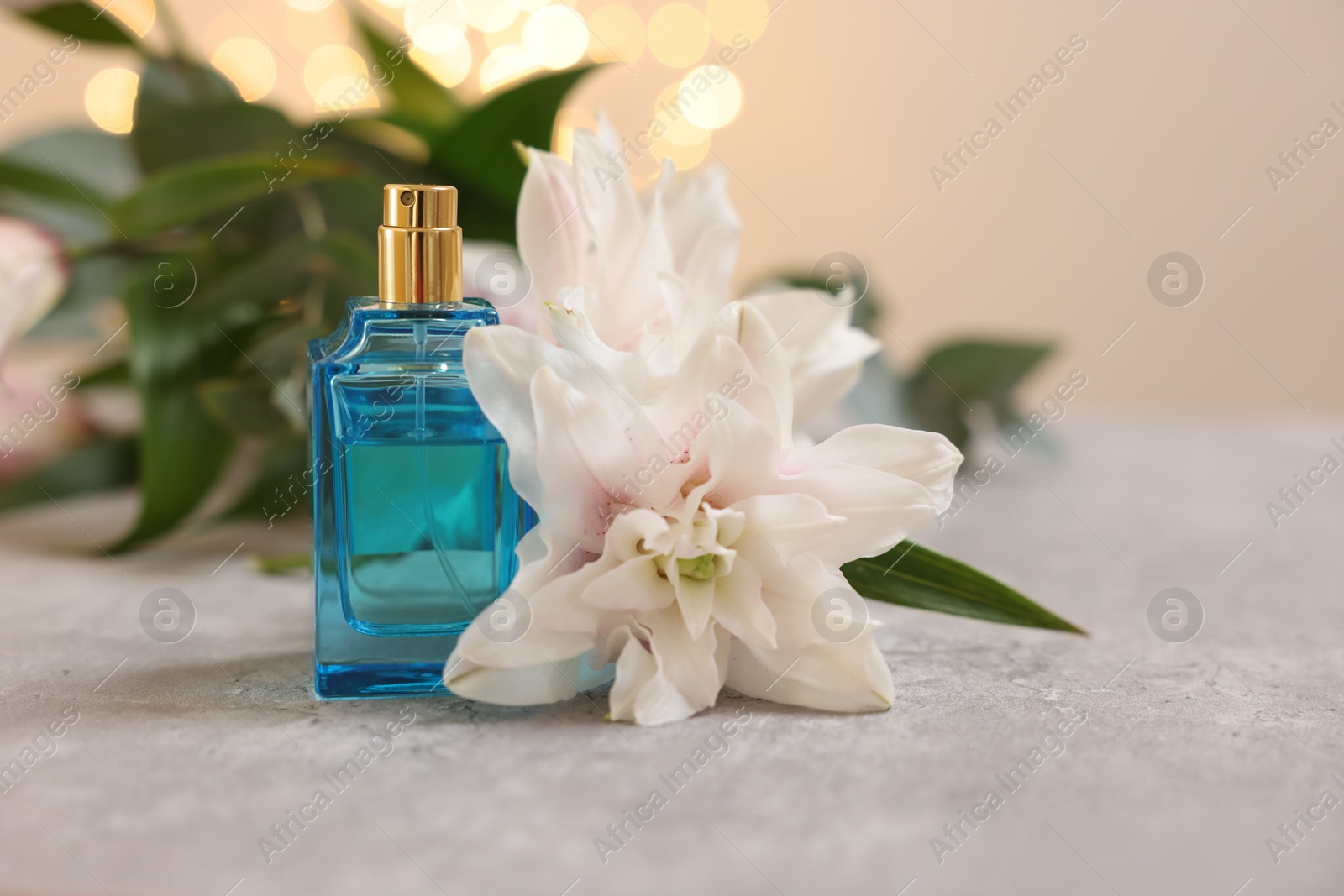 Photo of Bottle of perfume and beautiful lily flower on table against beige background with blurred lights, closeup