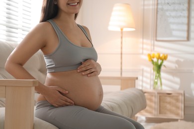 Photo of Pregnant young woman touching belly at home, closeup. Space for text