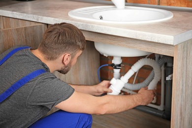 Professional plumber in uniform fixing sink indoors