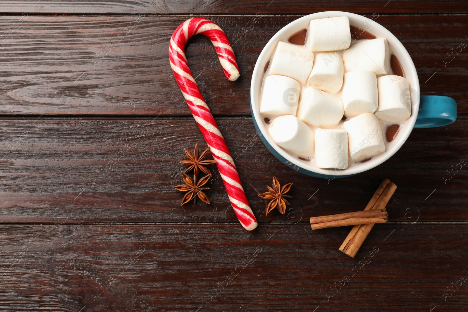 Photo of Tasty hot chocolate with marshmallows, candy cane and spices on wooden table, flat lay. Space for text