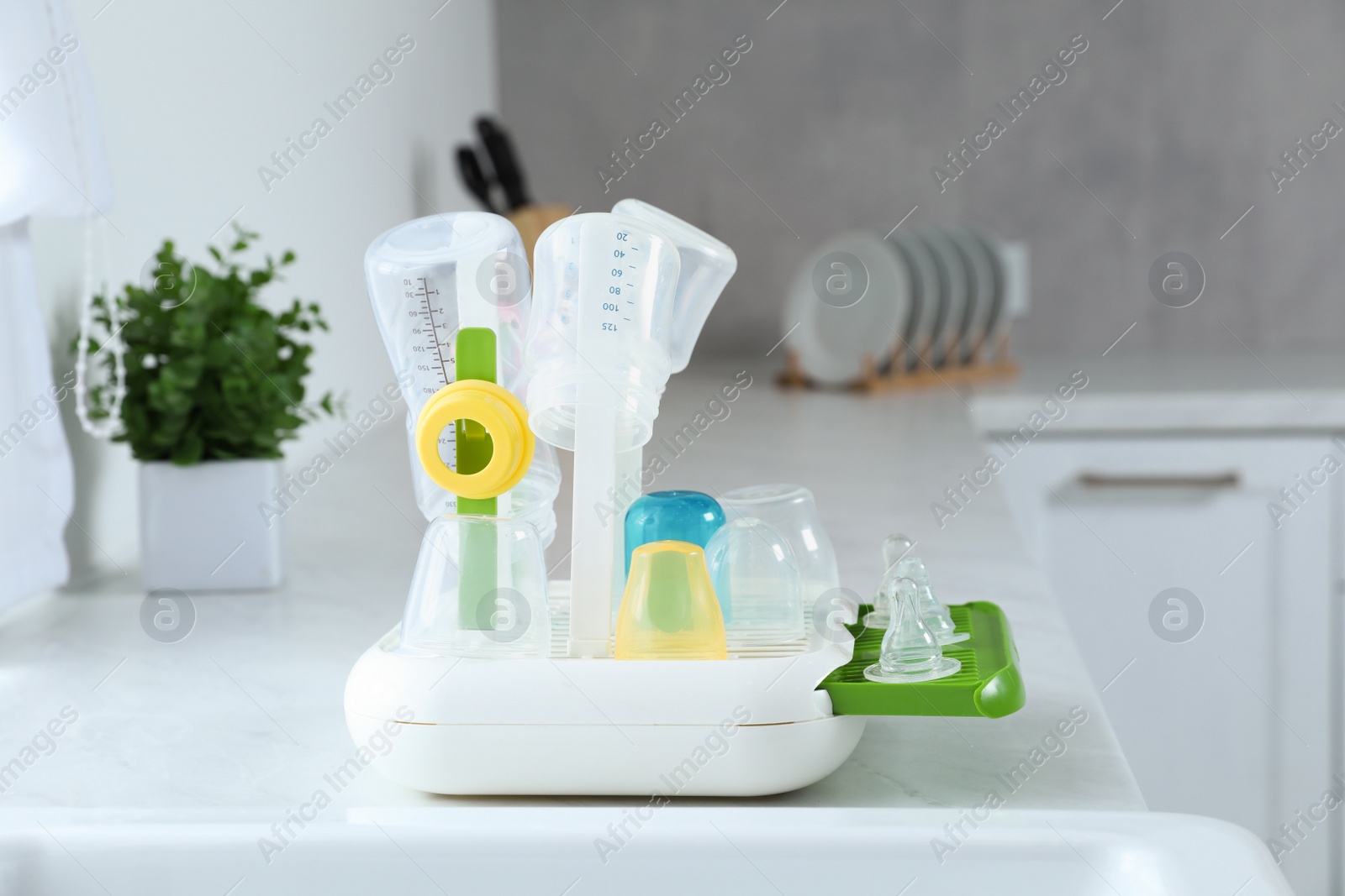 Photo of Dryer with baby bottles and nipples after sterilization on white countertop in kitchen