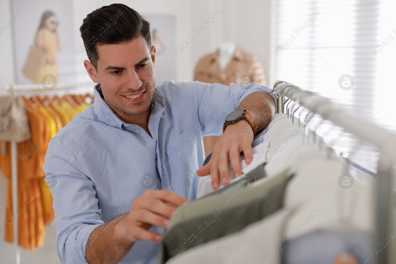 Photo of Man choosing clothes near rack in modern boutique