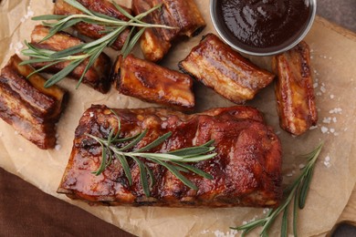 Photo of Tasty roasted pork ribs served with sauce and rosemary on table, top view