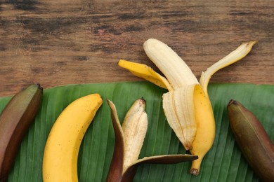 Different types of bananas and fresh leaf on wooden table, flat lay