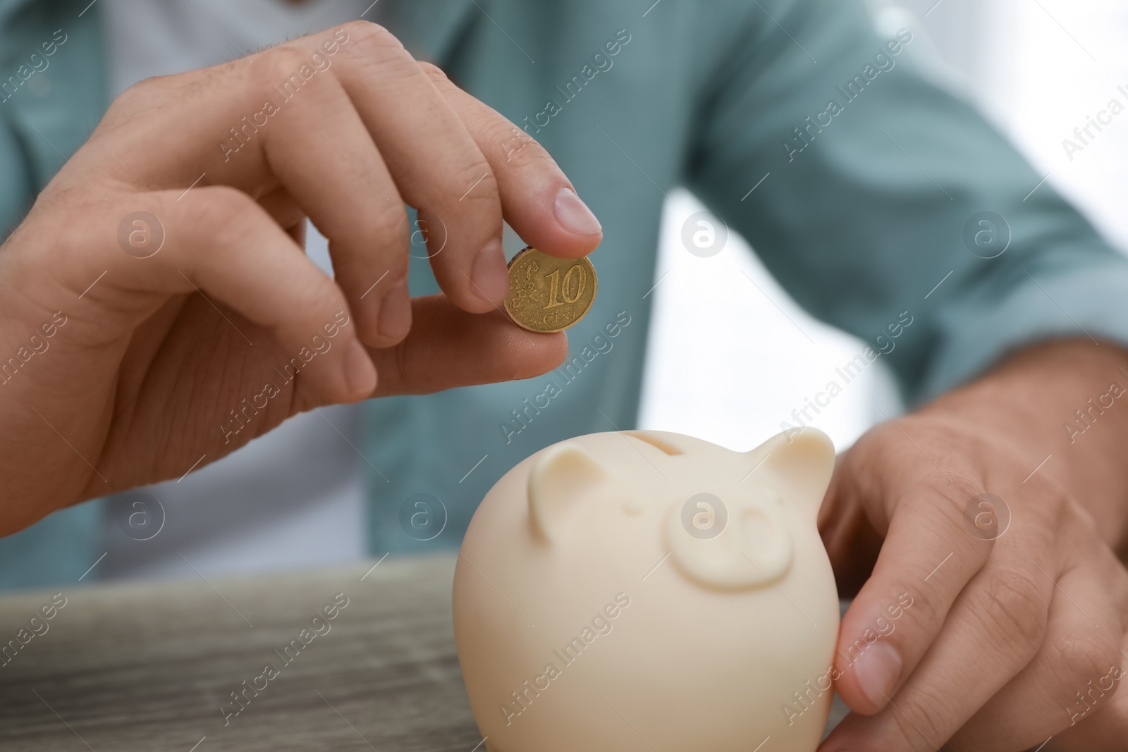 Photo of Man putting coin into piggy bank at wooden table, closeup