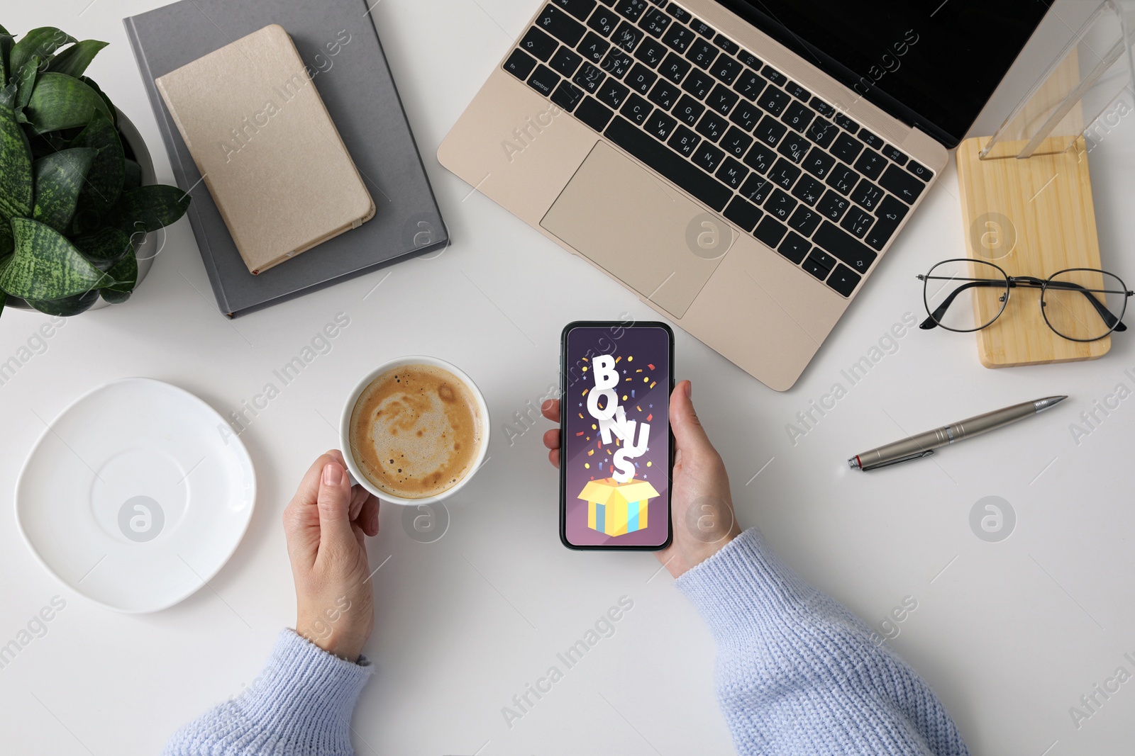 Image of Bonus gaining. Woman holding smartphone at white table, top view. Illustration of open gift box, word and confetti on device screen