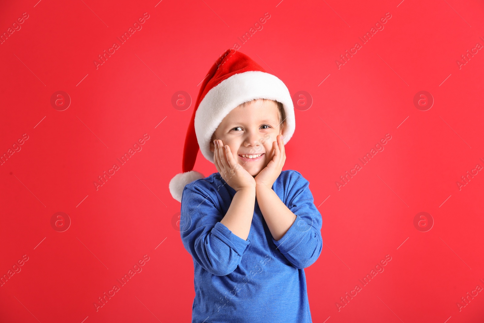 Photo of Cute little boy wearing Santa Claus hat on red background