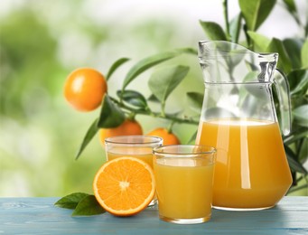 Image of Fresh orange juice on light blue wooden table in orchard. Space for text