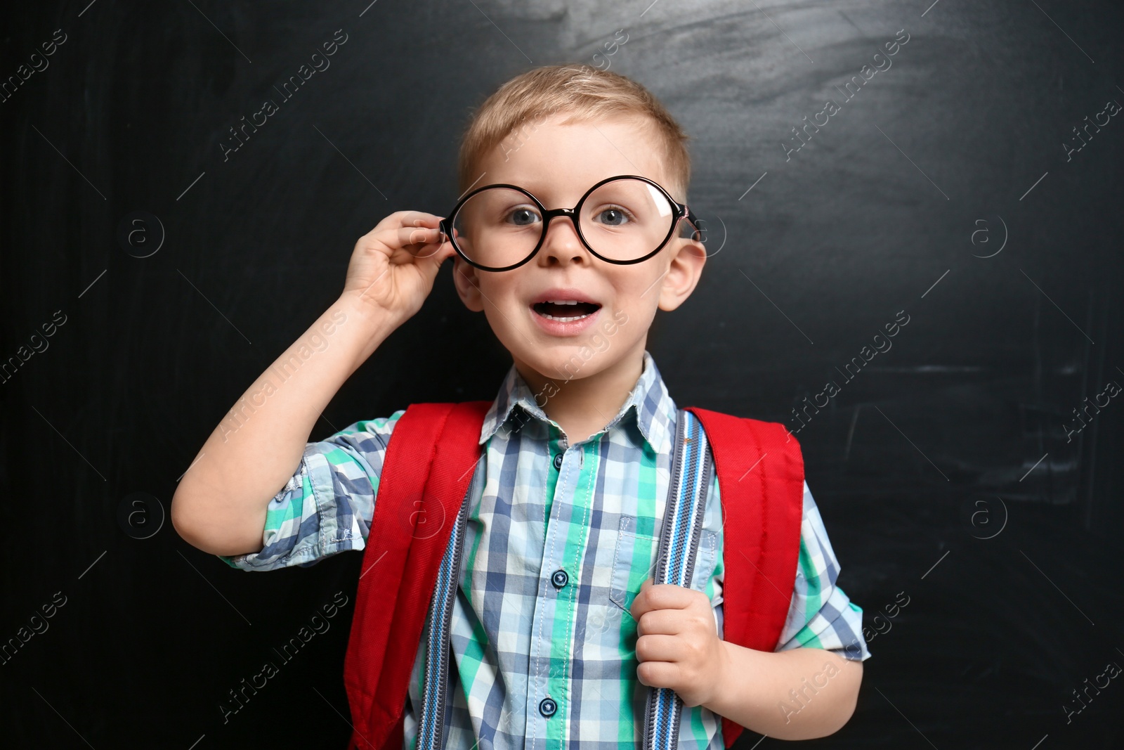 Photo of Cute little child wearing glasses near chalkboard. First time at school