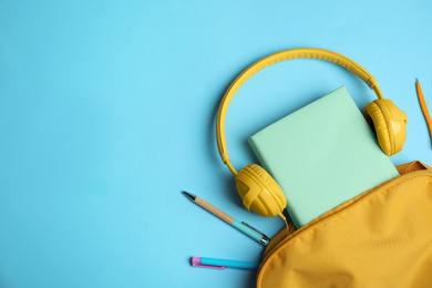 Flat lay composition with book and headphones on light blue background, space for text