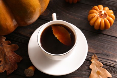 Cup of hot drink and pumpkin shaped candle on wooden table, closeup. Cozy autumn atmosphere