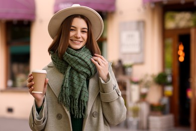 Photo of Beautiful woman in warm scarf with paper cup of coffee on city street