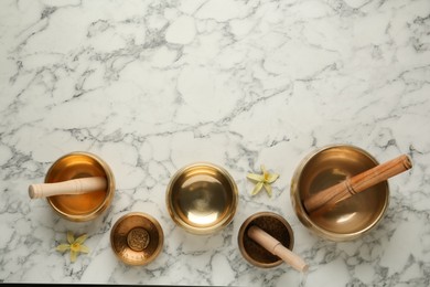 Golden singing bowls, mallets and flowers on white marble table, flat lay. Space for text