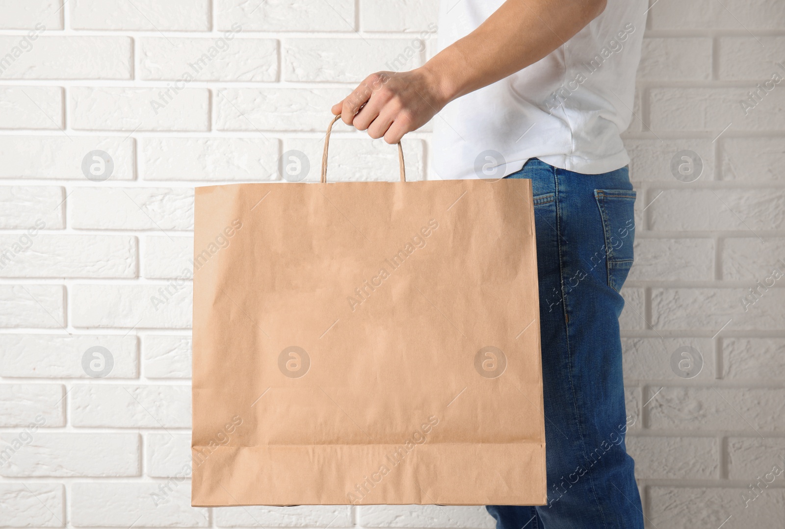 Photo of Man holding mock-up of paper shopping bag against wall