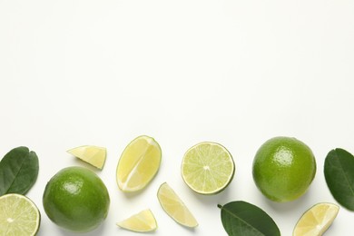 Photo of Whole and cut fresh ripe limes with green leaves on white background, flat lay