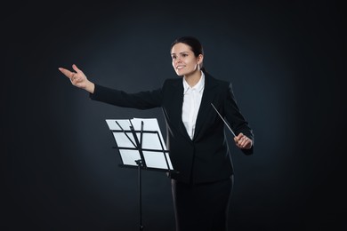 Photo of Happy young conductor with baton and note stand on dark background