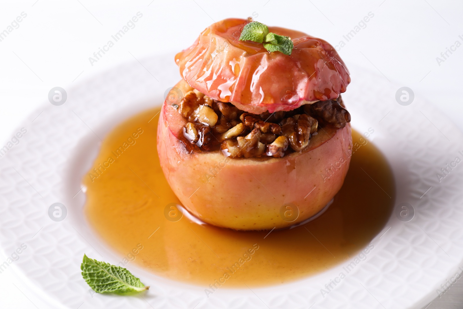 Photo of Tasty baked apple with nuts, honey and mint on white table, closeup